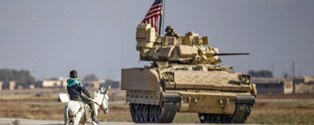 A boy rides his donkey next to a US Infantry Fighting Vehicle (IFV) patrolling near the village of Tal Alo, in the Yarubiyah district of Syria's northeastern Hasakah province near the M4 highway, on November 18, 2020. (Photo by Delil SOULEIMAN / AFP)