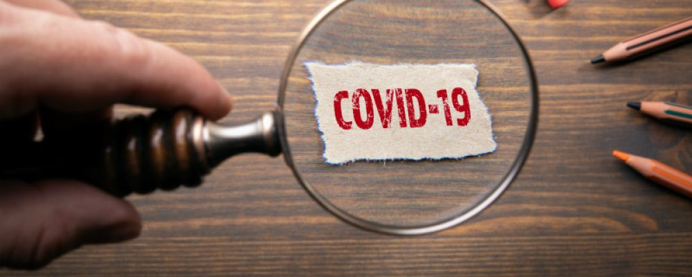 COVID-19. Exploring and explaining coronovirus - outbreak of desease that was first reported from Wuhan, China. Man's hand, holding magnifying glass