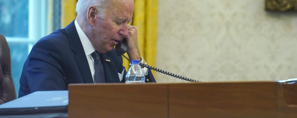 In this image made through a window, President Joe Biden talks on the phone with Ukrainian President Volodymyr Zelenskyy from the Oval Office of the White House in Washington, Thursday, Dec. 9, 2021. (AP Photo/Susan Walsh)